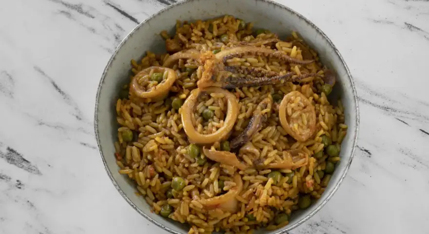 Un delicioso plato de arroz con calamares y guisantes, servido en un cuenco sobre una superficie de mármol.