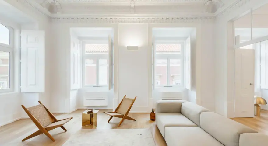 Ecco cosa fa l'architetto d'interni: crea un soggiorno minimalista con divano chiaro, sedie in legno e un tavolino dorato, valorizzando la luce naturale.