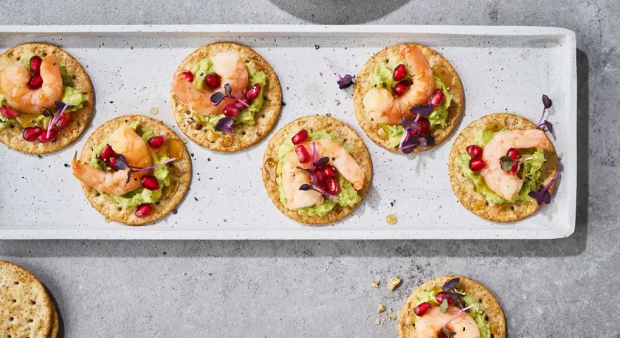 Mediterranes Fingerfood kalt: Garnelen auf Avocado-Creme mit Granatapfelkernen und Kräutern auf Crackern.
