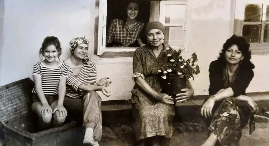 Maria Wojewodzka z rodziną na tle domu. Kobiety w różnym wieku, jedna z nich trzyma kwiaty.