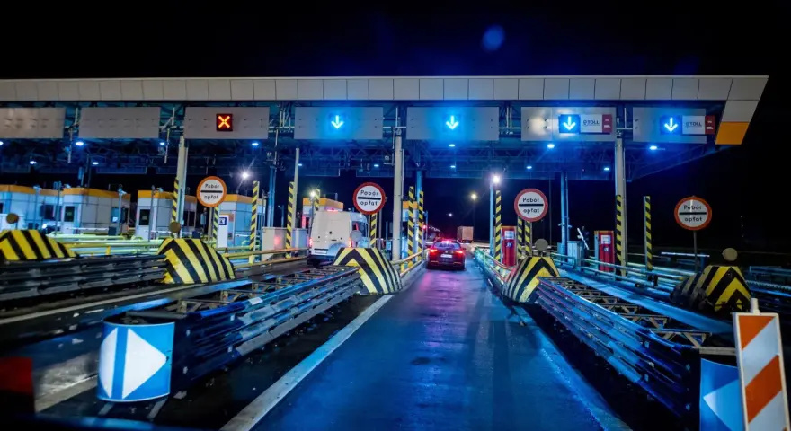 Nocny widok na bramki autostradowe z niebieskimi światłami i znakami, samochody wjeżdżają na płatne pasy.
