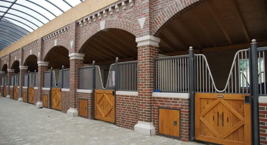 Belle écurie pour chevaux avec des boxes en briques rouges, des portes en bois et un toit transparent.