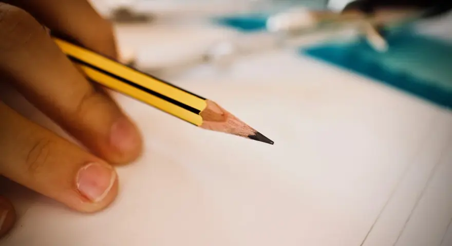 Dłoń trzymająca ołówek nad kartką papieru, symbol wsparcia w edukacji, w tym dla osób ze specjalnymi potrzebami edukacyjnymi.