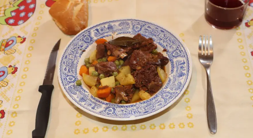 Un plato de corzo guisado con patatas, zanahorias y guisantes, acompañado de pan y vino tinto. ¡Una de las mejores recetas de corzo guisado!