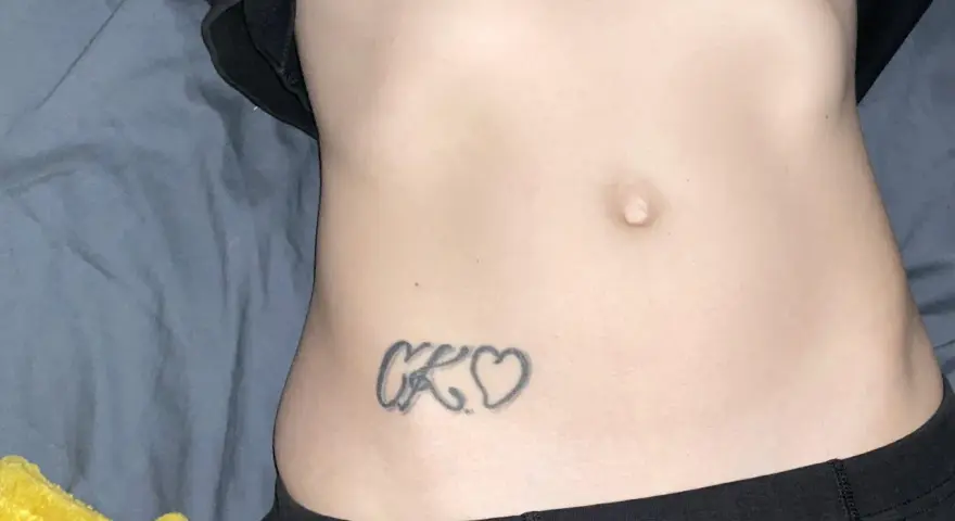 Tatuaz inicjaly CK wplecione w serduszka na brzuchu.