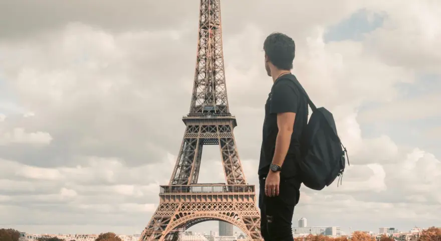 Un joven con mochila admira la Torre Eiffel. Quizás piensa que es dificil aprender francés, pero París es hermoso.
