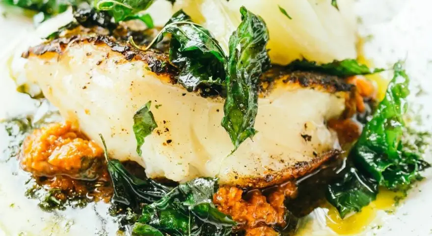 Delicioso bacalao al pil pil, con su piel dorada, acompañado de verduras frescas y una salsa vibrante.