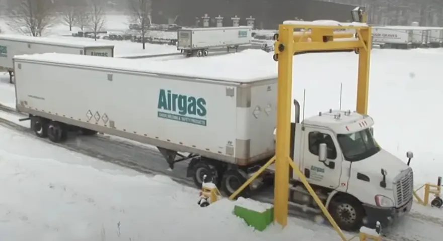 Ciężarówka z naczepą Airgas pod żółtą bramownicą w śnieżny dzień.