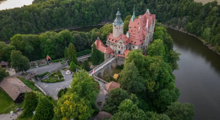 Zamek Czocha, malowniczo położony na skalistym cyplu nad rzeką, otoczony bujną zielenią.