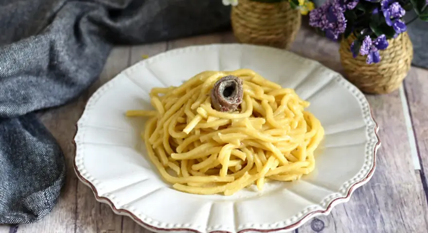 Un piatto di pasta burro e alici, condita con un tocco di sapore marino, servita su un piatto bianco decorato.