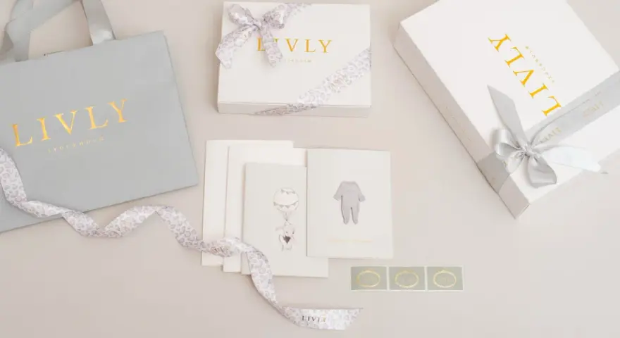 En nyfödd present box från Livly Stockholm med en grå påse, vita boxar med guldig text och leopardmönstrat band. Kort med illustrationer av en elefant och en babybody.