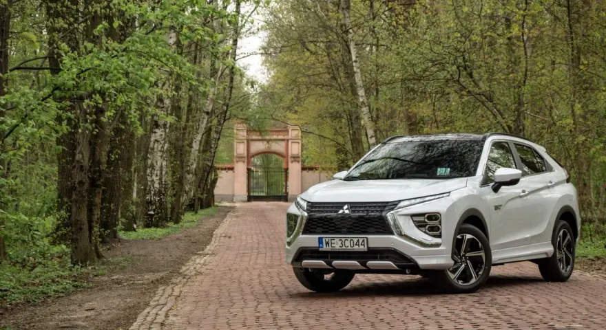 Biały Mitsubishi Eclipse Cross na tle bramy i drzew. Wiele pozytywnych mitsubishi eclipse cross opinie potwierdza jego wszechstronność.