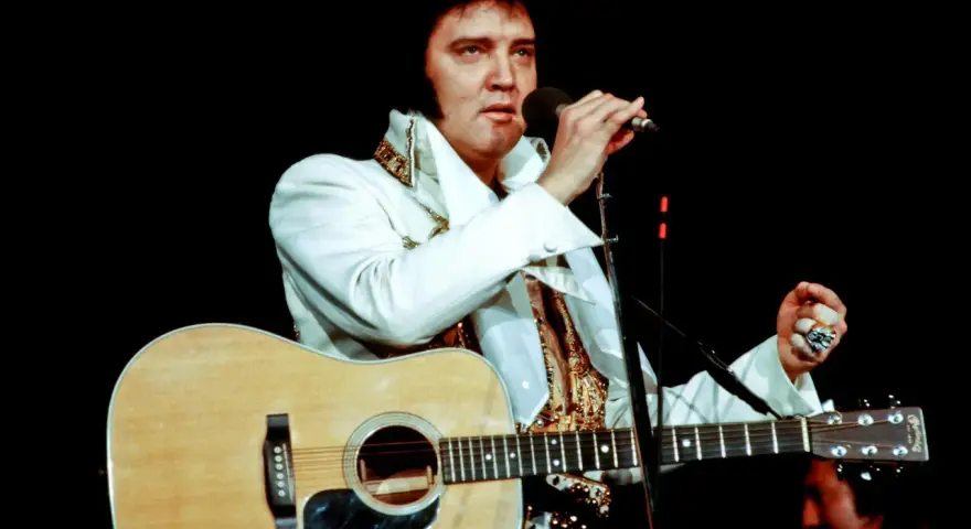 Elvis Presley singt mit Gitarre und Mikrofon, ein Bild, das sein immenses Vermögen symbolisiert.
