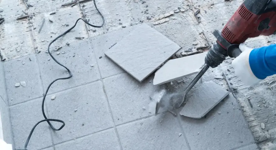 Skuwanie płytek młotem udarowym. Widać fragmenty rozbijanej podłogi i kabel zasilający.