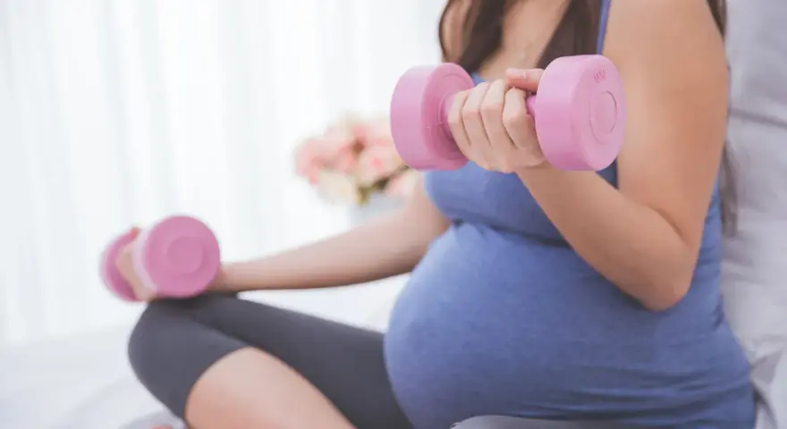 Ciężarna kobieta wykonuje ćwiczenia z hantlami, przygotowując się do porodu.