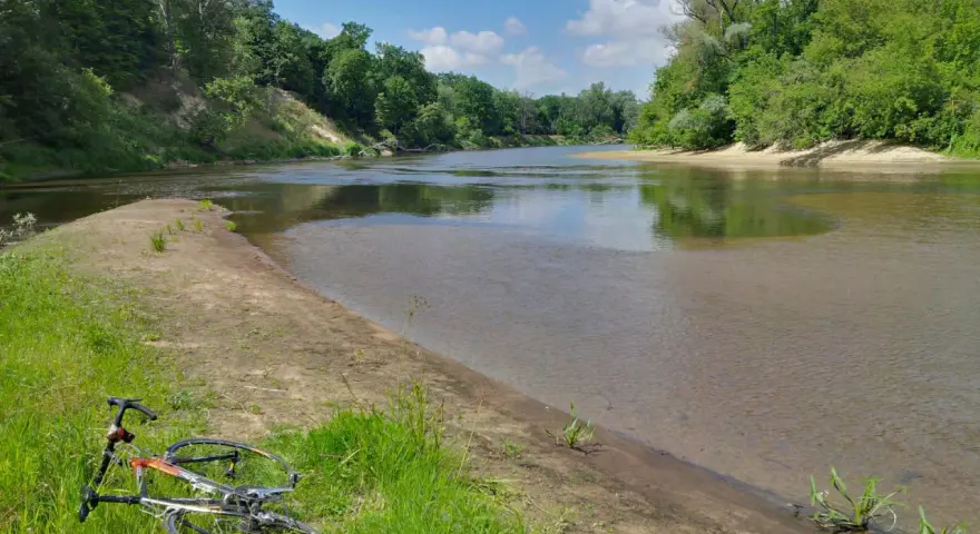 Rower leży na trawie nad rzeką, otoczoną zielenią. To malowniczy zakątek, prawdziwa szwajcaria podlaska.