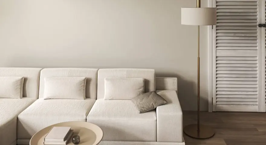 Divano modulare color tortora, tavolino ovale con libri, lampada da terra dorata e porta a soffietto in legno.