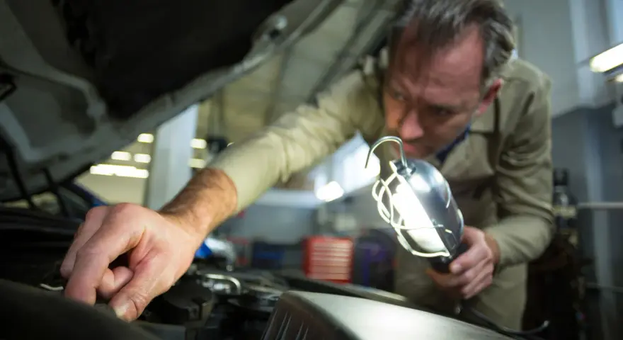 Meccanico controlla il motore con una lampada per capire se la batteria auto è da cambiare.