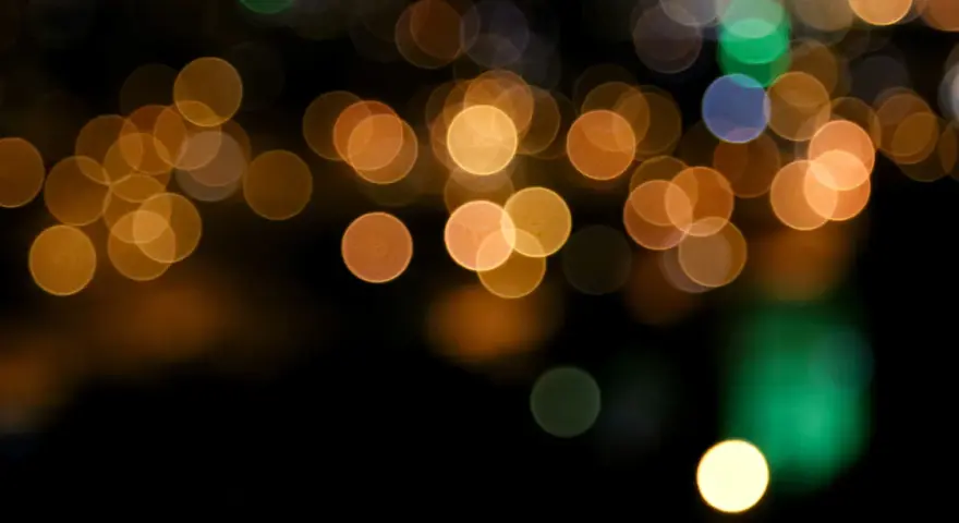 Des lumières de ville floues créent un arrière-plan bokeh chaleureux, avec des cercles dorés, verts et bleus sur fond noir.
