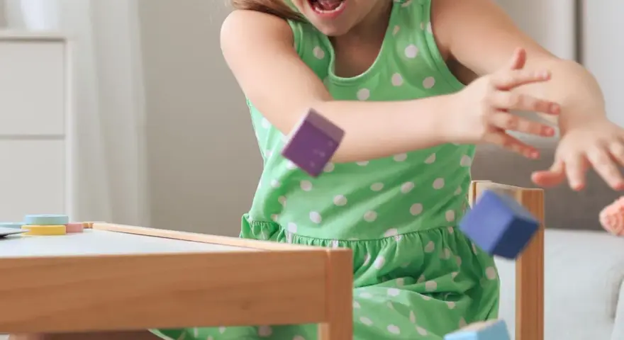 Ein Mädchen in einem grünen Kleid wirft bunte Holzklötze. Ein Versuch, laute Kinder zur Ruhe zu bringen, indem man sie zum Spielen anregt.