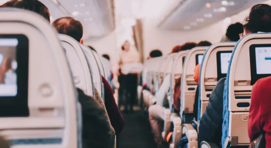 View from inside an airplane cabin, showing rows of seats with passengers and entertainment screens.
