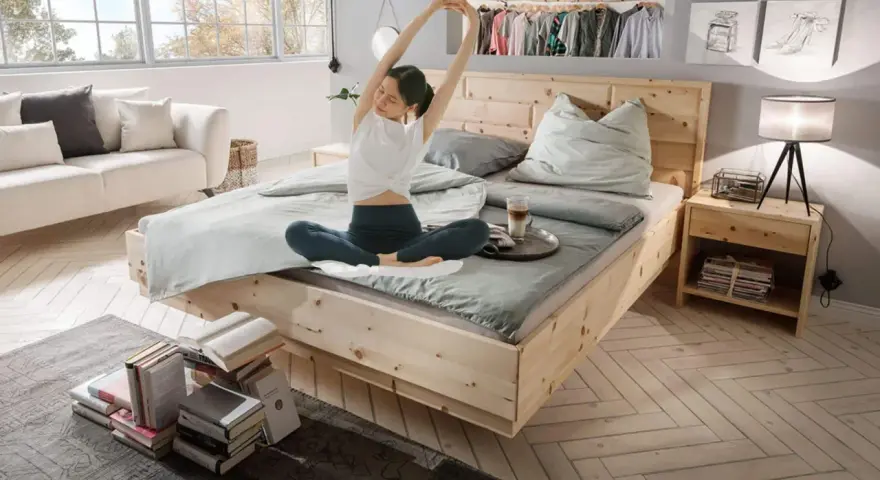Frau dehnt sich im hellen Schlafzimmer. Ein gemütliches Bett, ein Sofa und Bücher laden zum Entspannen ein. Perfekt, um das Schlafzimmer einzurichten.