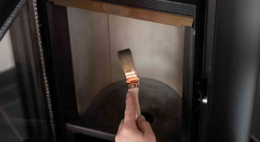 Mano con pennello per pulire il vetro della stufa bruciato.