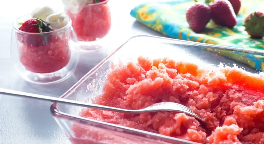 Erfrischende Erdbeer Granita in einer Glasschale, garniert mit frischen Erdbeeren und Sahne in kleinen Gläsern.