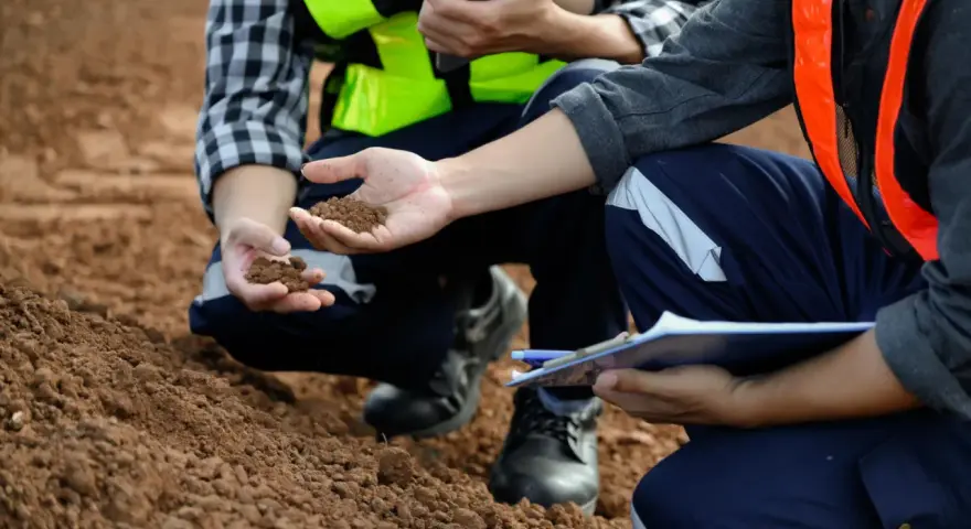 Pracownicy w kamizelkach odblaskowych analizują próbki ziemi, wykonując badania geotechniczne gruntu.