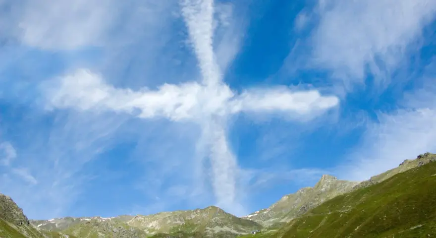 Ein Kreuz aus Wolken am blauen Himmel über grünen Bergen. Man könnte sagen, ihr werdet Zeichen am Himmel sehen.