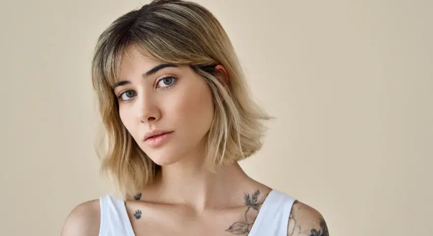 Kobieta z tatuażami na ramionach i dekolcie, z modną fryzurą long bob i grzywką.