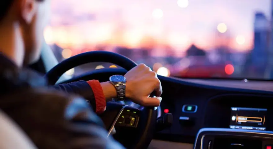 Uomo al volante, con un orologio al polso, pronto per un nuovo uber lavoro al tramonto.