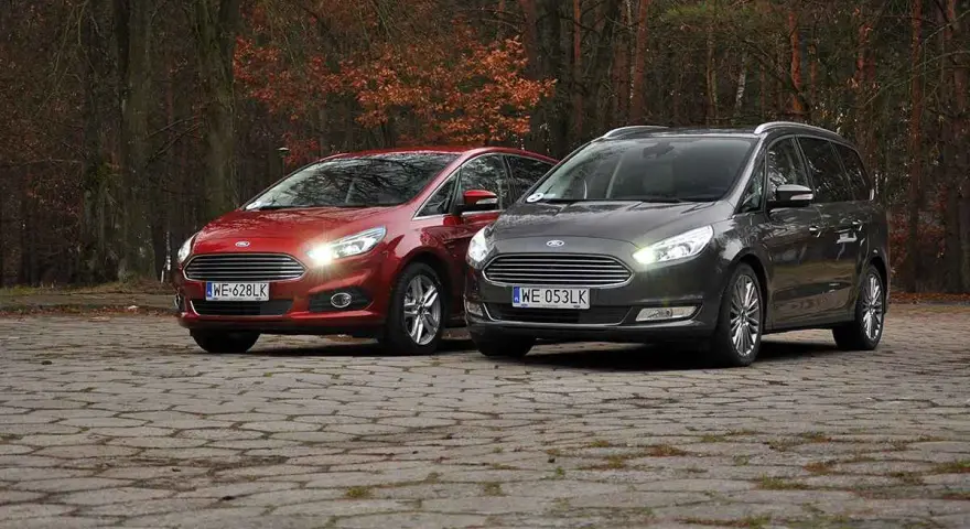 Dwa samochody Ford, czerwony S-Max i szary Galaxy, stoją na brukowanej nawierzchni w jesiennym lesie.