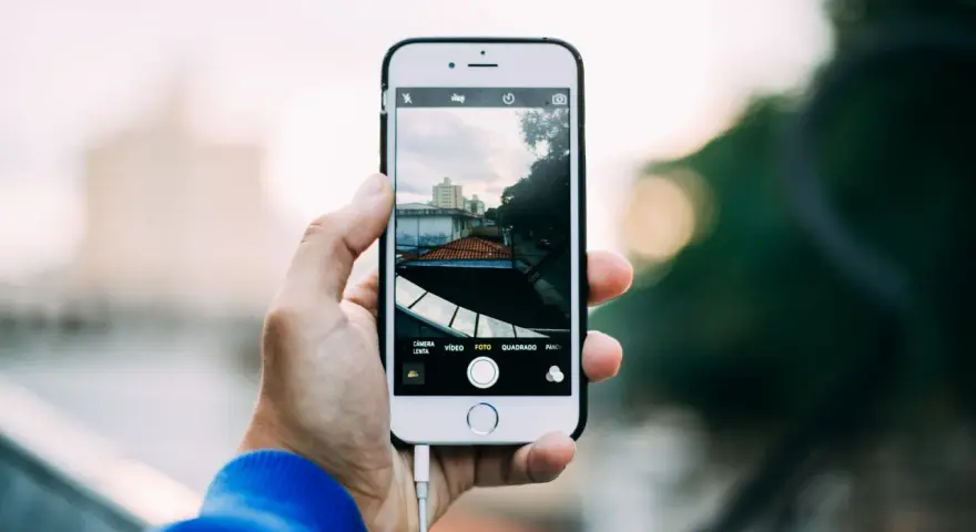 Dłoń trzyma iPhone'a, pokazując ekran z widokiem miasta. Dowiedz się, jak robic zdjecia iphonem, by uchwycić takie ujęcia.