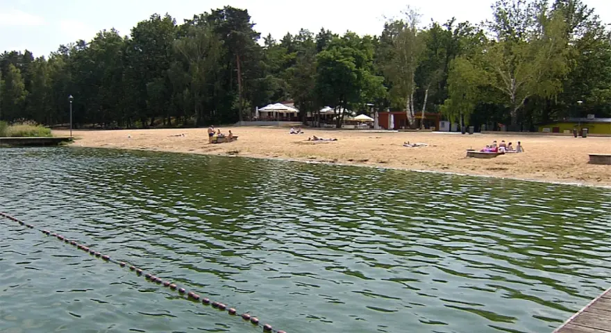Plaża nad jeziorem Szperek, z kilkoma osobami odpoczywającymi na piasku i wodą w tle.