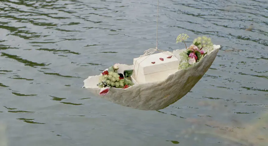 Ein Schiffchen mit Blumen und einer Schachtel schwimmt auf dem Wasser. Eine würdevolle Idee für Kinderbeerdigungen.