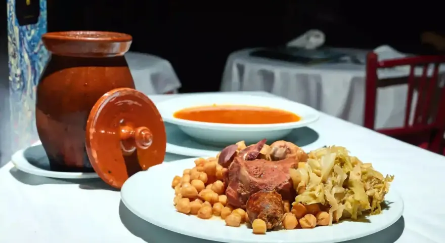 Plato de cocido madrileño con garbanzos, carne, repollo y sopa en un cuenco.