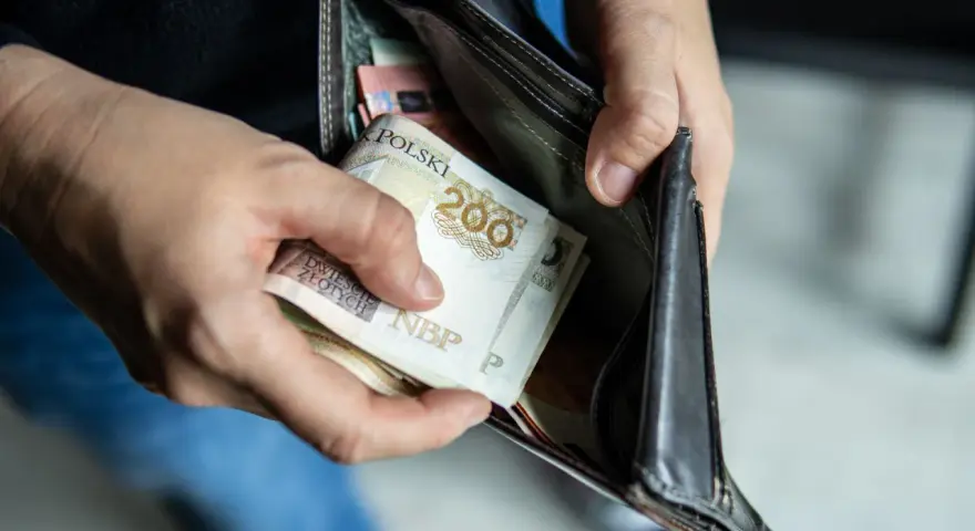 Ręce wkładają polskie banknoty 200 zł do portfela. Czy można mieć dwóch komorników na pensji, gdy pieniędzy jest tak mało?