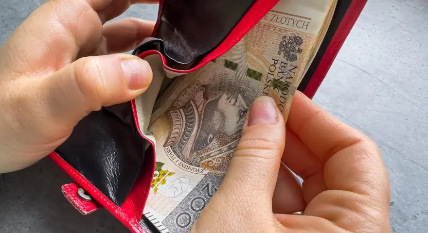 Ręce wkładają banknoty do czerwonego portfela. To może być 1000 zł na drugie dziecko, wsparcie dla rodziny.