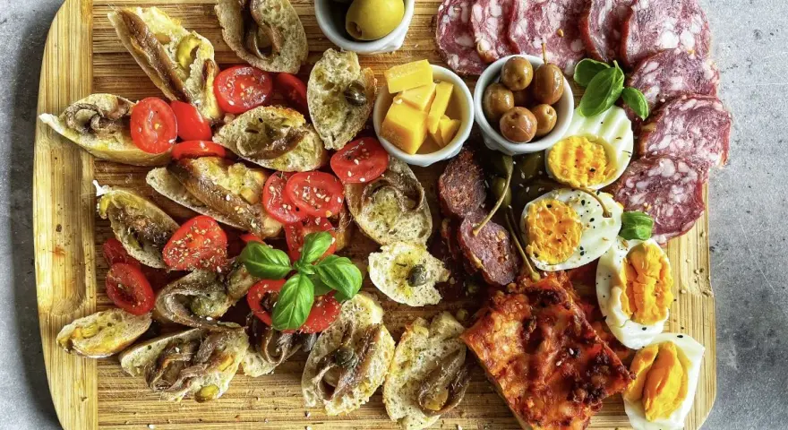 Kaltes italienisches Fingerfood: Bruschetta mit Sardellen, Tomaten, Oliven, Käse, Eiern und Salami auf Holzbrett.