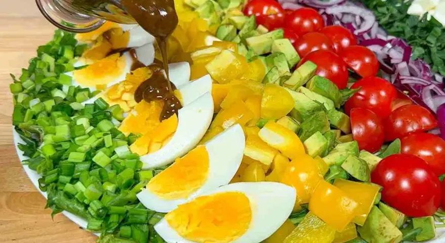 Un'insalata di avocado colorata con uova sode, pomodorini, peperoni gialli e cipolla rossa, condita con una salsa scura.