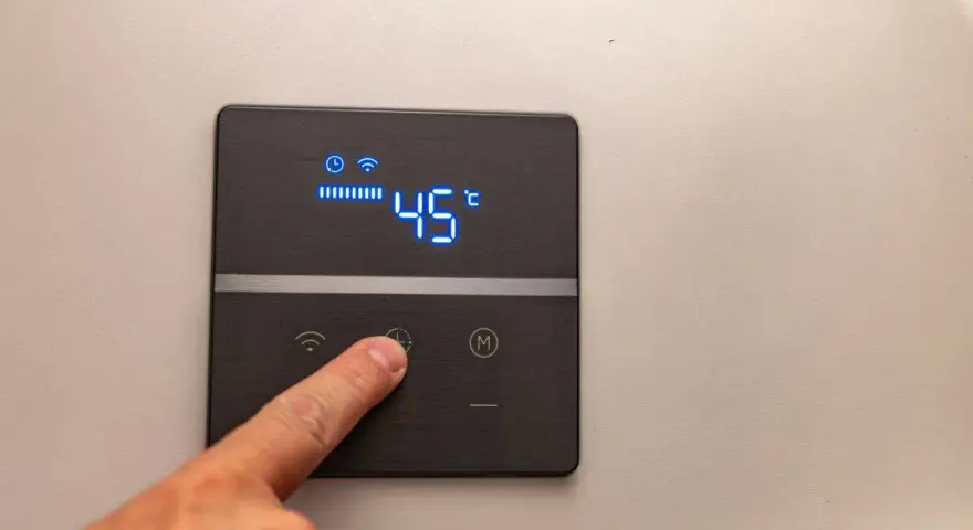 Dito, un dito preme il pulsante di un pannello digitale che mostra l'indicatore temperatura scaldabagno a 45°C, con icone Wi-Fi e di riscaldamento attive.