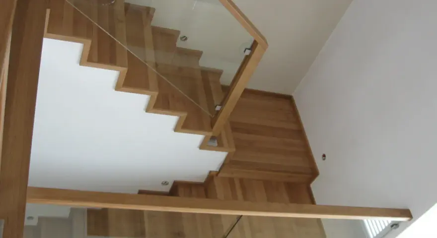 Nowoczesne schody dywanowe na beton, z drewnianymi stopniami i szklaną balustradą, tworzą lekkość i elegancję.