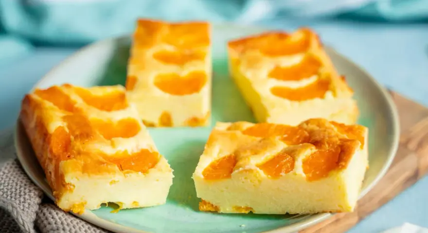 Vier Stücke saftiger Mandarinen Quark Kuchen auf einem Teller, garniert mit frischen Mandarinenstücken.