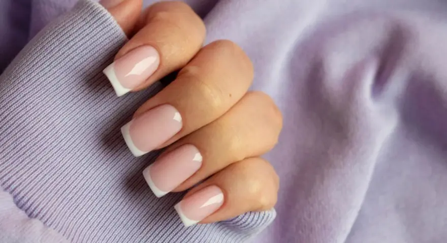 Dłoń z paznokciami w stylu french kolor, na tle lawendowej bluzy. Klasyka i elegancja.
