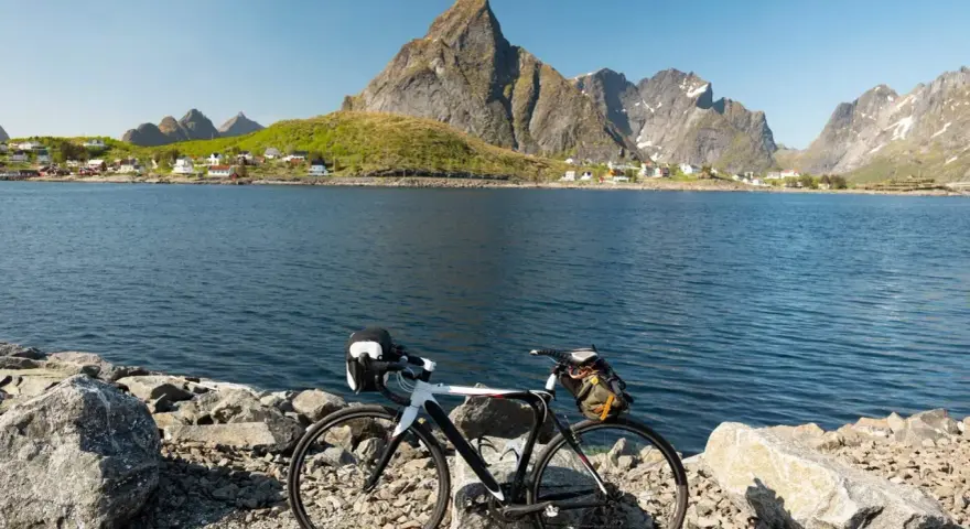 En cykel står vid en sjö med berg och en by i bakgrunden. Perfekt för mtb norge-äventyr.