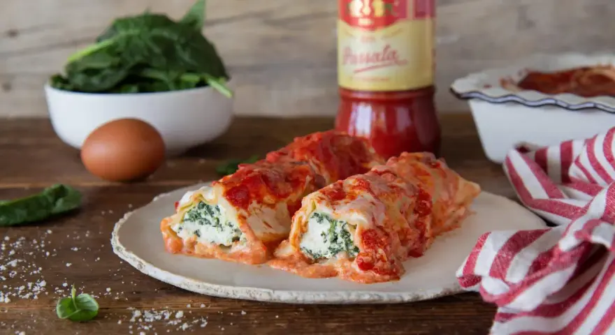 Cannelloni ricotta e spinaci fumanti, conditi con passata Mutti e formaggio filante, pronti per essere gustati.