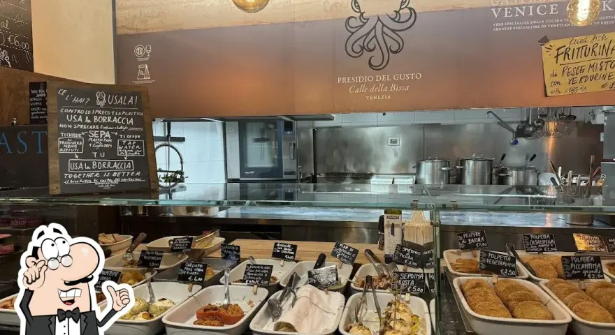 A display case filled with small dishes of food, with a chalkboard menu and a restaurant logo in the background.