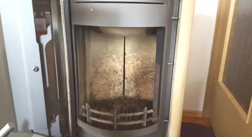 Innenraum eines Ofens mit einem vertikalen Riss im schamottstein gebrochen. Asche und Ruß bedecken den Boden und die Wände.