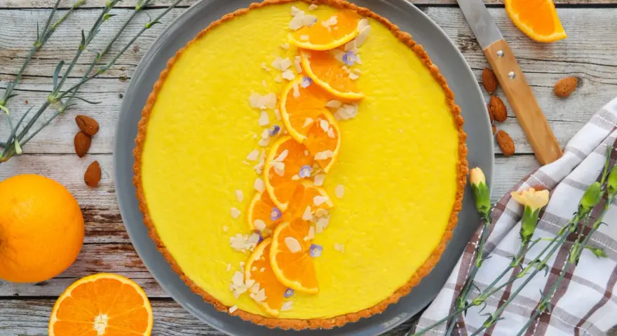 Une délicieuse tarte à l'orange, garnie de fines tranches d'orange, d'amandes effilées et de petites fleurs bleues. Un régal visuel et gustatif.